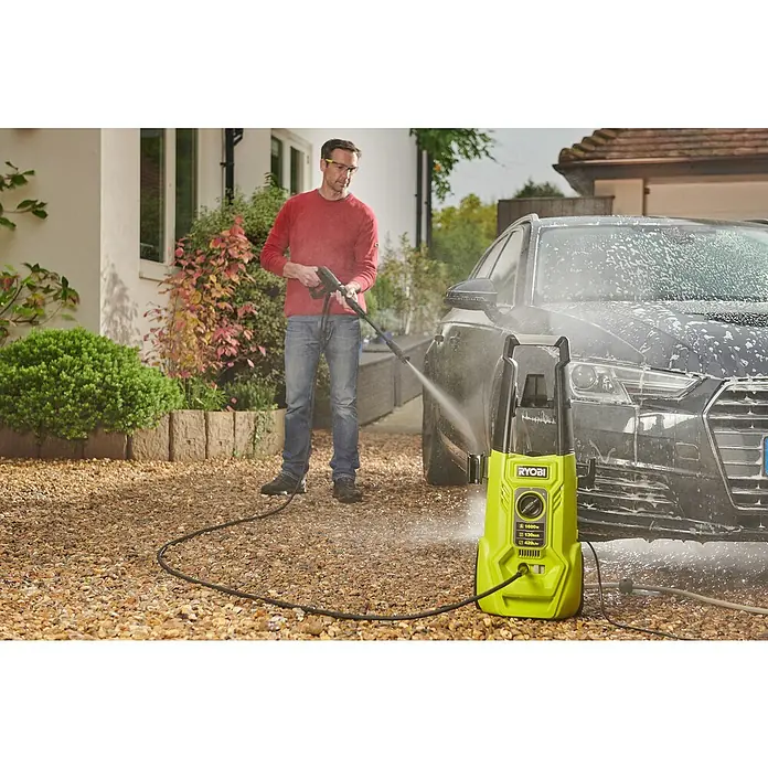 Ryobi Hochdruckreiniger RY130PWA - 1.600 W - Ein Mann benutzt einen Ryobi Hochdruckreiniger, um ein Auto zu waschen. Der gelb-schwarze Reiniger steht im Vordergrund.