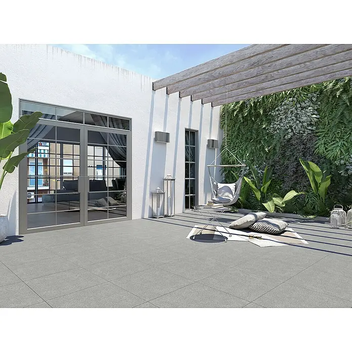 Terrassenfliese Padang 2.0 - 100 x 100 x 2 cm, Dunkelgrau, Matt - Blick auf eine moderne Terrasse mit grauem Fliesenboden, Pergola, Grünpflanzenwand und einem hängenden Stuhl, der zum Entspannen einlädt.