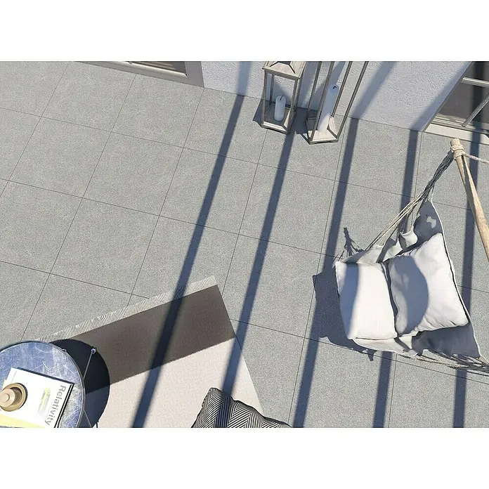 Terrassenfliese Padang 2.0 - 100 x 100 x 2 cm, Dunkelgrau, Matt - Gartenterrasse mit grauen Bodenfliesen, einem bequemen Hängesessel mit Kissen und einem stilvollen Beistelltisch mit Buch für entspannte Stunden im Freien.