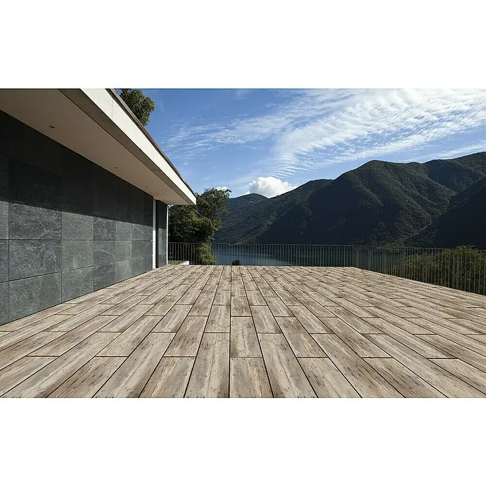 Terrassenfliese Skandinavia 2.0 - 40 x 120 x 2 cm, Grau/Beige, Matt - Eine moderne Holzterrasse mit Blick auf malerische Berge und einen ruhigen See unter einem strahlend blauen Himmel mit leichten Wolken.