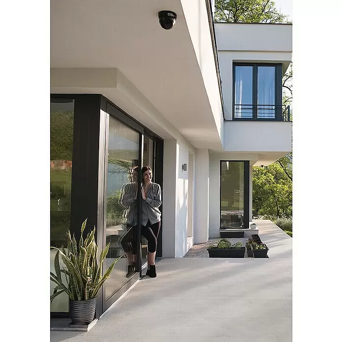 Terrassenfliese Revesto 2.0 - 60 x 60 x 2 cm, Grau, Matt - Schwarze Dome-Sicherheitskamera, an der Decke eines modernen Gebäudeaußenbereichs montiert.