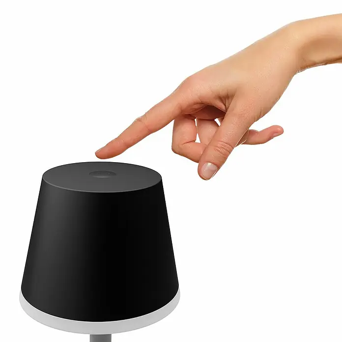 Philips Hue Akku-Tischleuchte Go Portable - 6,2 W, L x B x H: 21,9 x 20,9 x 38,8 cm, Mehrfarbig, Schwarz - Finger berührt eine moderne, schwarze Tischleuchte mit einem schlanken, minimalistischen Design und einem sanften Lichteffekt.