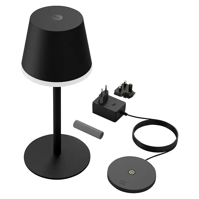 Philips Hue Akku-Tischleuchte Go Portable - 6,2 W, L x B x H: 21,9 x 20,9 x 38,8 cm, Mehrfarbig, Schwarz - Das Bild zeigt eine Philips Hue Tischleuchte mit Zubehör wie Netzteilen und einem Dimmschalter, alles in einem modernen, minimalistischen Design.