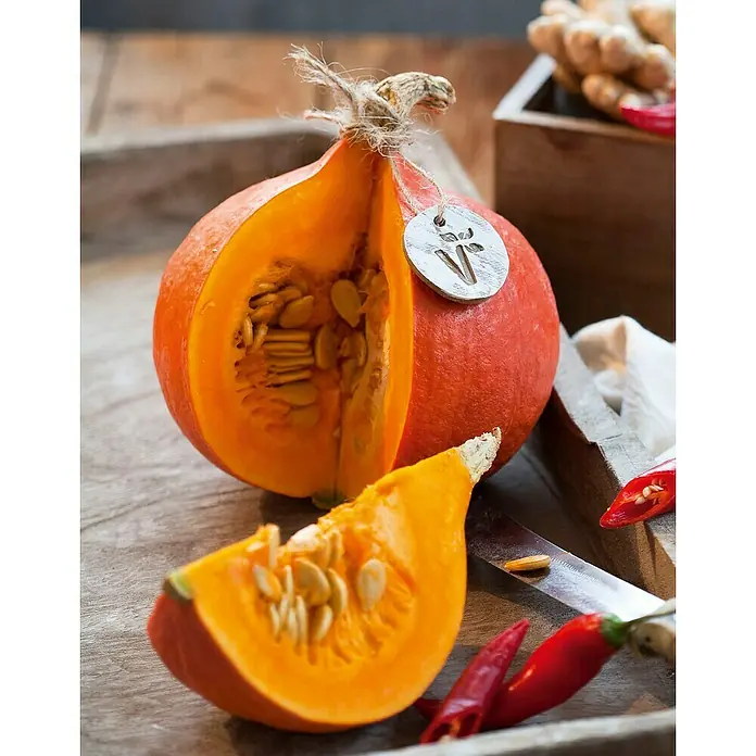 Piardino Riesen-Kürbis - 10,5 cm, Erntezeit: August - Ein angeschnittener Hokkaido-Kürbis mit Samen, der auf einem Holztablett zusammen mit Chilis liegt.