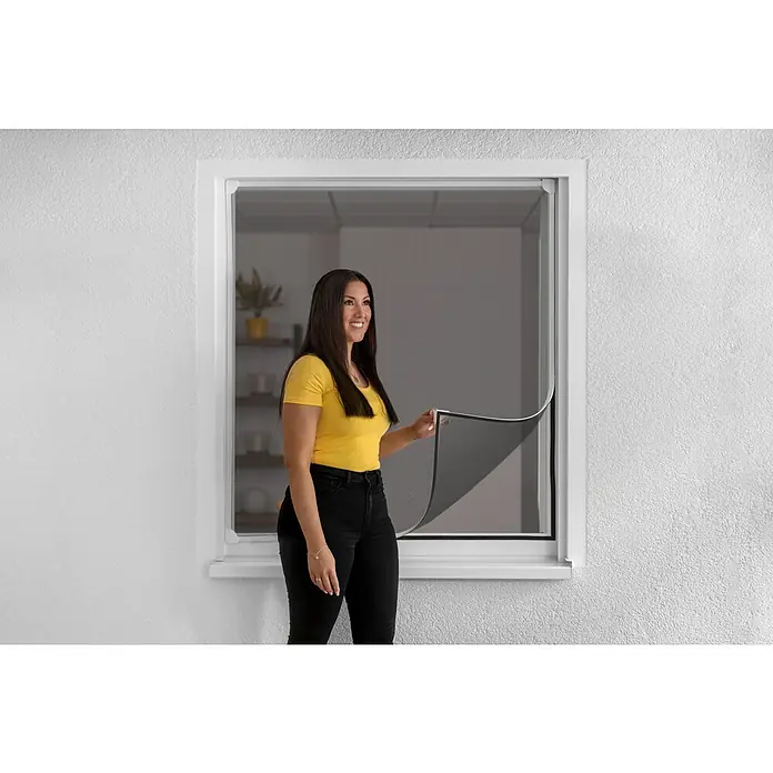 Schellenberg Mosquitera - An x Al: 130 x 150 cm, Montaje de la mosquitera: Fijación magnética, Color bastidor: Blanco - Mujer muestra una mosquitera enrollable en un marco de ventana, que ofrece protección contra insectos y fácil operación.
