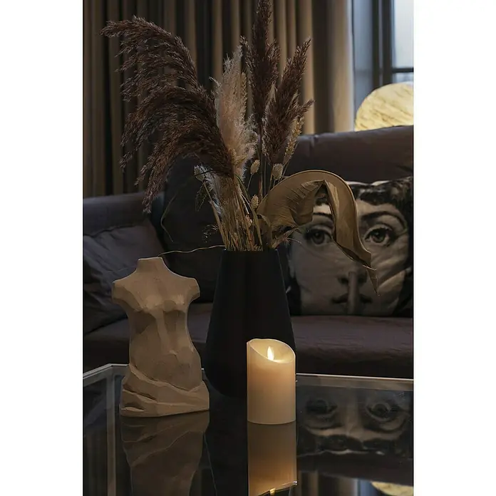 Konstsmide LED-Kerze - Beige, Wachs, 7,6 x 11,4 cm - Stillleben auf einem Couchtisch mit einer weiblichen Torsoskulptur, einer Kerze und einer Vase mit Trockenblumen.