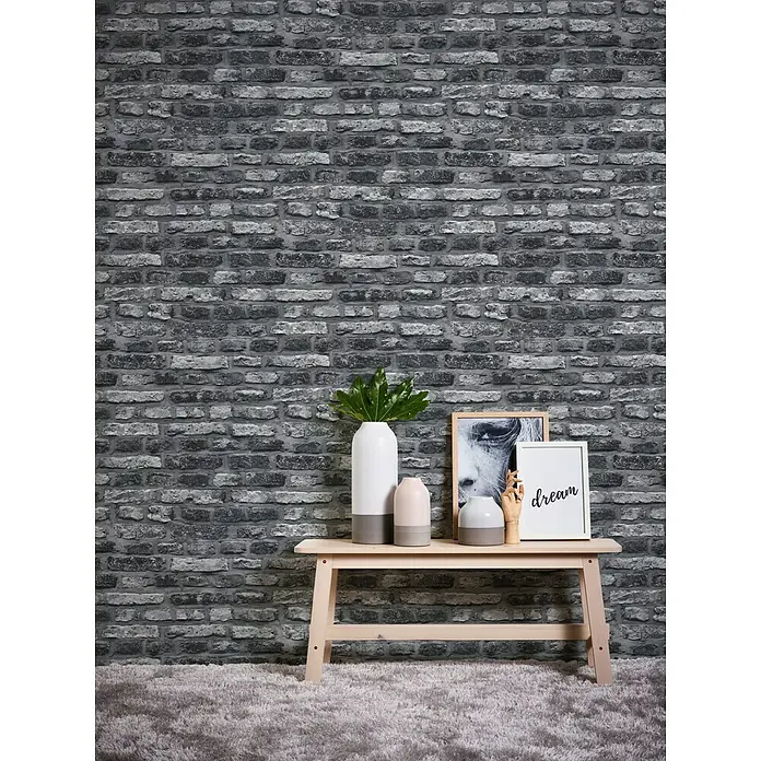 A.S. Création Il Decoro Vliestapete Steine - Schwarz/Weiß, Steinoptik, 10,05 x 0,53 m - Dekorative Inneneinrichtung mit einer gemusterten Ziegelwandtapete, einem hellen Holztisch, Vasen und einem gerahmten Bild, das eine elegante und gemütliche Atmosphäre schafft.