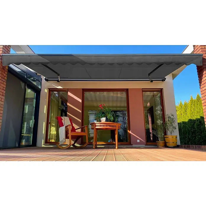SM Gelenkarmmarkise T-5406/107Grau, Farbe Gestell: Anthrazitgrau, Breite: 5 m, Ausfall: 3 m - Graue Markise über einer Terrasse mit Holzdeck, Möbeln und Pflanzen, die Schatten spendet.