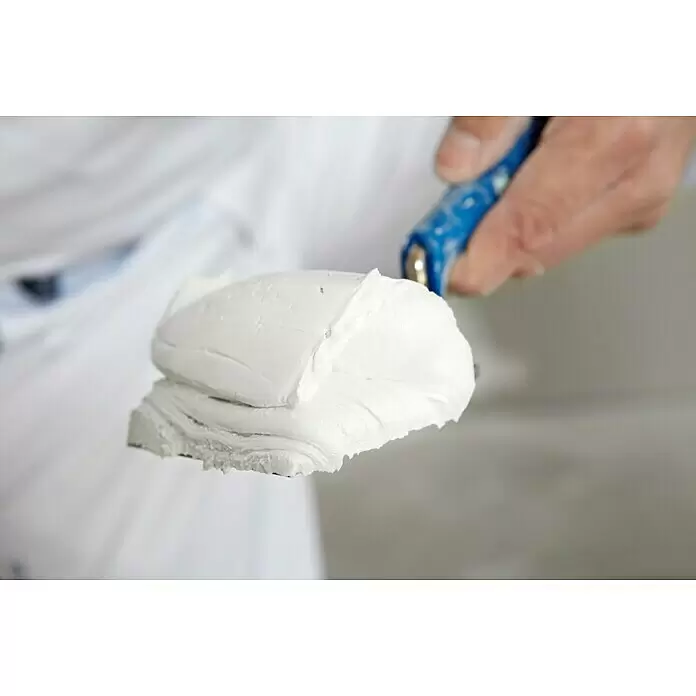 Rigips VARIO Fugenspachtel Finish - 18 kg - Hand hält einen Spachtel, beladen mit weißem Putz/Spachtelmasse.