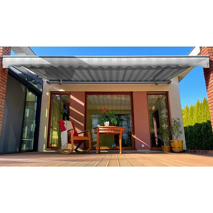 SM Gelenkarmmarkise REC-089 - Hellgrau/Grau, Farbe Gestell: Weißaluminium, Breite: 3,6 m, Ausfall: 2,5 m - Graue Markise über einer Terrasse mit Tisch, Stuhl und Pflanzen, die Schatten spendet und eine gemütliche Atmosphäre schafft.