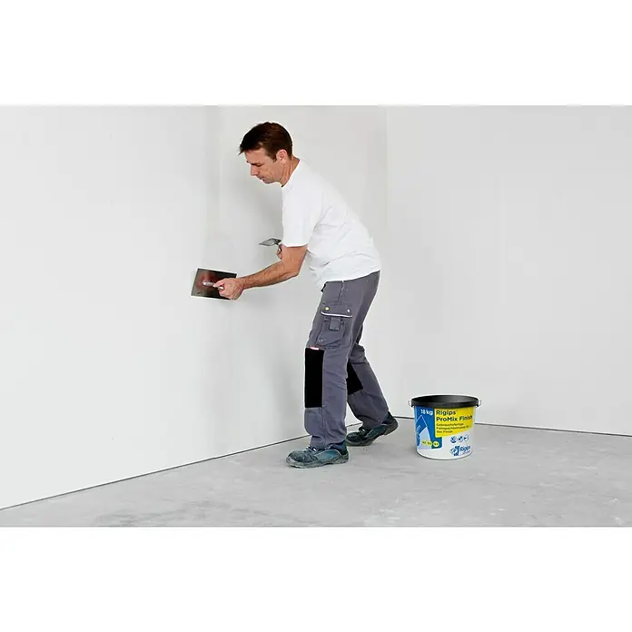 Rigips VARIO Fugenspachtel Finish - 18 kg - Ein Mann glättet eine Wand mit Rigips ProMix Finish. Zu sehen ist ein Eimer Rigips ProMix Finish mit 18kg Inhalt im Raum.