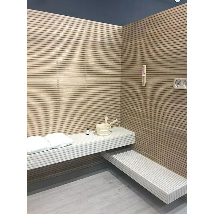 Wandfliese Spa Beige Dekor - 30 x 90 cm, Beige, Matt - Eine Sauna mit hölzernen Bänken, einem Holzeimer und einem Thermometer an der Wand. Entspannung pur im eigenen Zuhause.