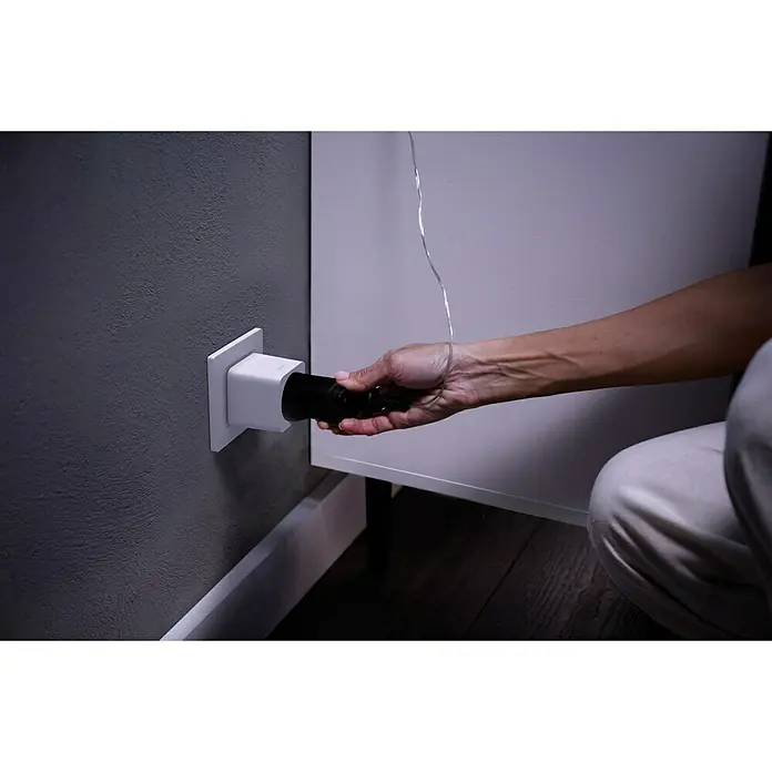 Philips Hue Funksteckdose Plug - Weiß, Max. Anschlussleistung: 2.300 W, 1 Stk. - Ein Elektriker schliesst einen schwarzen Stecker an eine weisse Steckdose mit Überspannungsschutz an einer grauen Wand an.