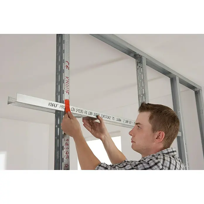 Knauf UA-Aussteifungsprofil - 2.600 x 75 x 40 mm - Ein Mann montiert ein Knauf Profil, das mit einer roten Klemme an einer Metallstruktur befestigt ist.