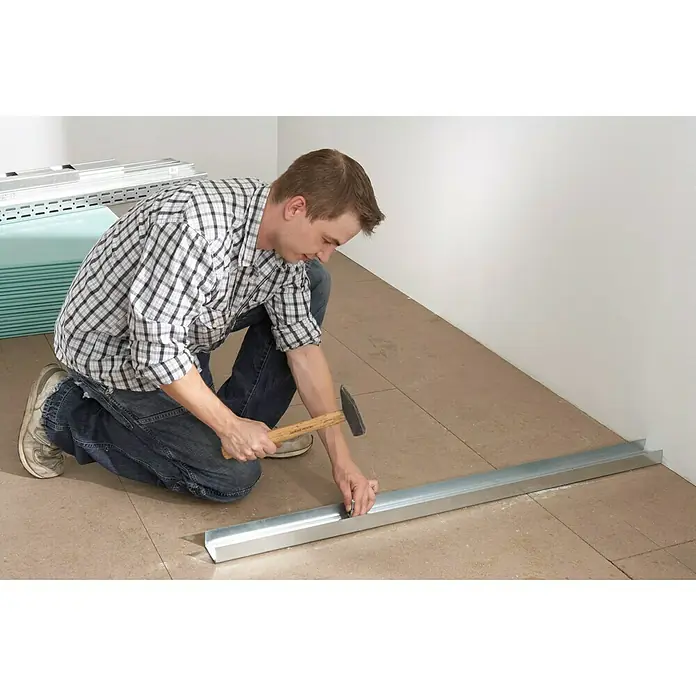 Knauf UW-Rahmenprofil - 4.000 x 100 x 40 mm, Stahl - Mann befestigt Metallschiene mit Hammer am Boden. Die Metallschiene ist das Hauptprodukt.
