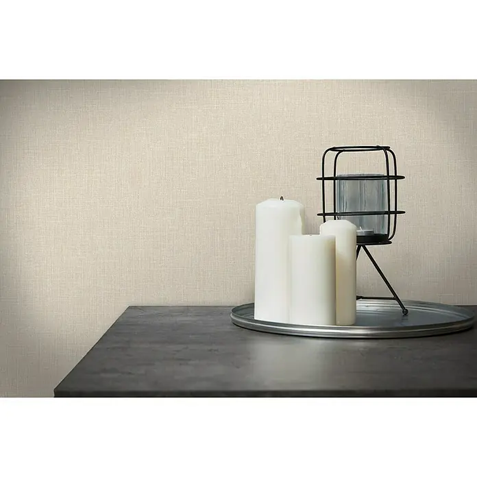 A.S. Création Metropolitan Stories Vliestapete Textil-Optik - Beige, Uni, 10,05 x 0,53 m - Kerzenarrangement mit weißen Kerzen und einer Laterne auf einem eleganten, dunklen Tisch vor einer strukturierten Wand.