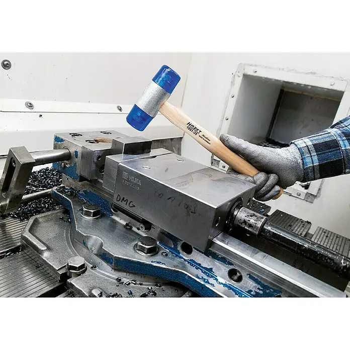 Hazet Schonhammer 1951-32 - Durchmesser Kopf: 32 mm - Ein Hazet Schonhammer 1951-35 in Aktion, ideal für präzise Arbeiten ohne Beschädigung der Werkstücke. Der Hammer liegt auf einer Werkbank mit Metallspänen.