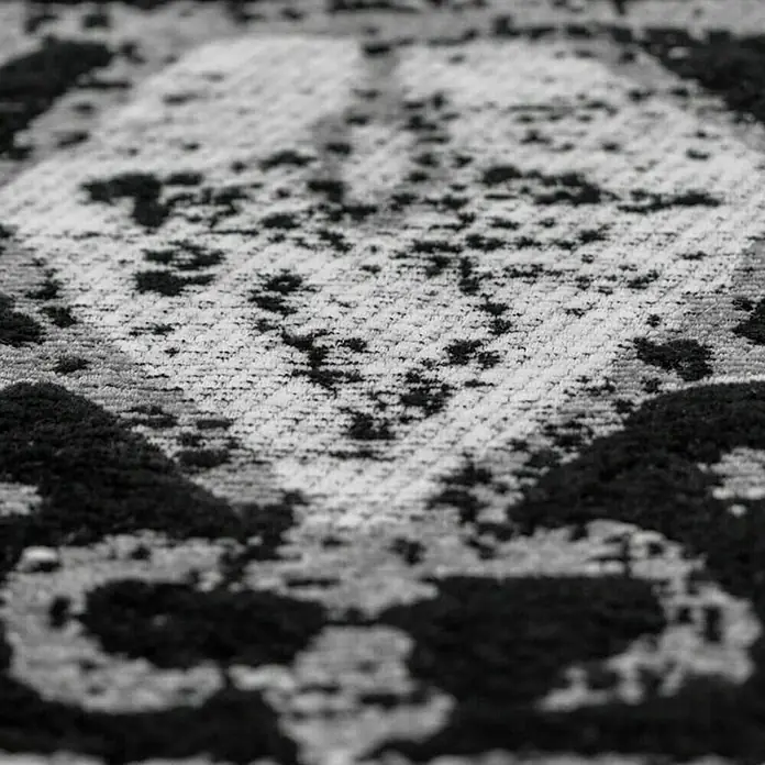Kayoom Flachgewebeteppich River 150 - Schwarz/Grau, 150 x 80 cm, 70 % Baumwolle, 30 % Polyester - Nahaufnahme eines gemusterten Teppichs in Schwarz-Weiß, der eine interessante Textur und ein abstraktes Design aufweist.
