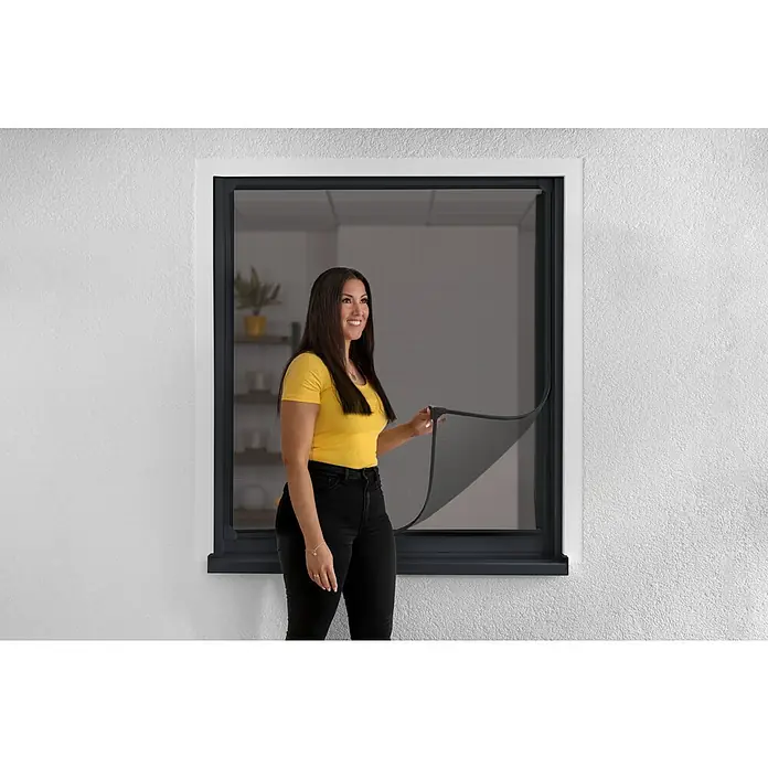 Schellenberg Insect Stop Mosquitera Flex - An x Al: 130 x 150 cm, Montaje de la mosquitera: Fijación magnética, Color bastidor: Antracita - Mujer abriendo una ventana equipada con una mosquitera magnética, que ofrece una fácil protección contra insectos y buena circulación del aire.