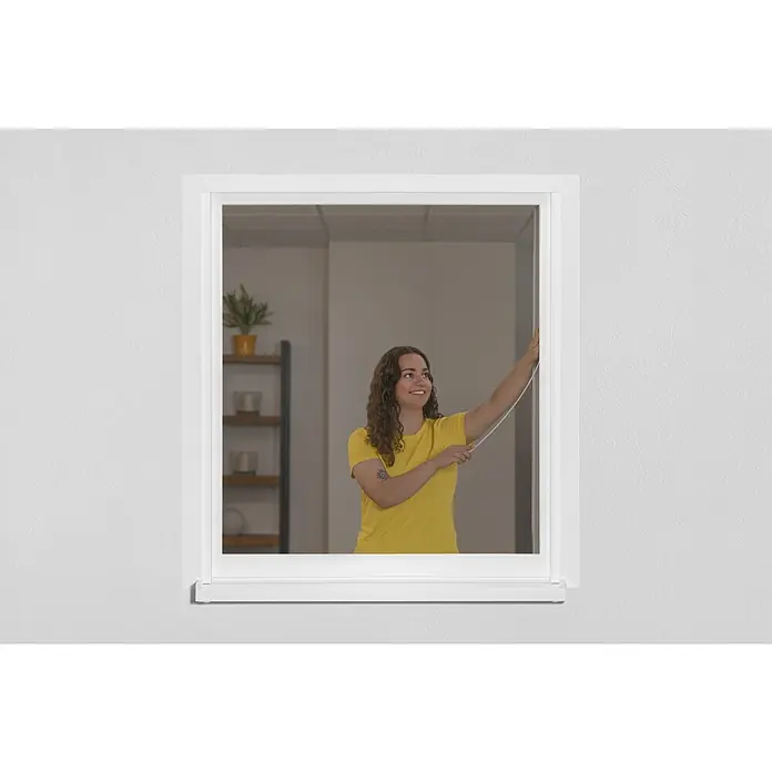 Schellenberg Mosquitera para ventana EasyClick - An x Al: 130 x 150 cm, Montaje de la mosquitera: Pinzas, Color bastidor: Blanco - Mujer accionando un estor enrollable opaco en un marco de ventana blanco, que proporciona privacidad y protección solar.