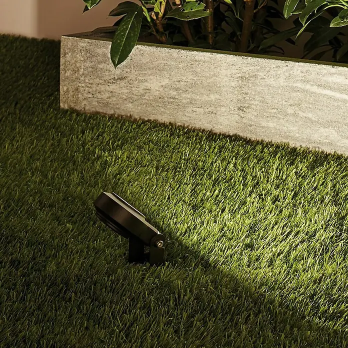 Paulmann Plug & Shine LED-Gartenspot Sting - 6 W, 24 V, Erdspieß, Höhe: 29 cm - Bild einer dunklen Gartenleuchte auf Rasen neben einem Pflanzgefäß, die eine subtile Beleuchtung für den Außenbereich bietet.