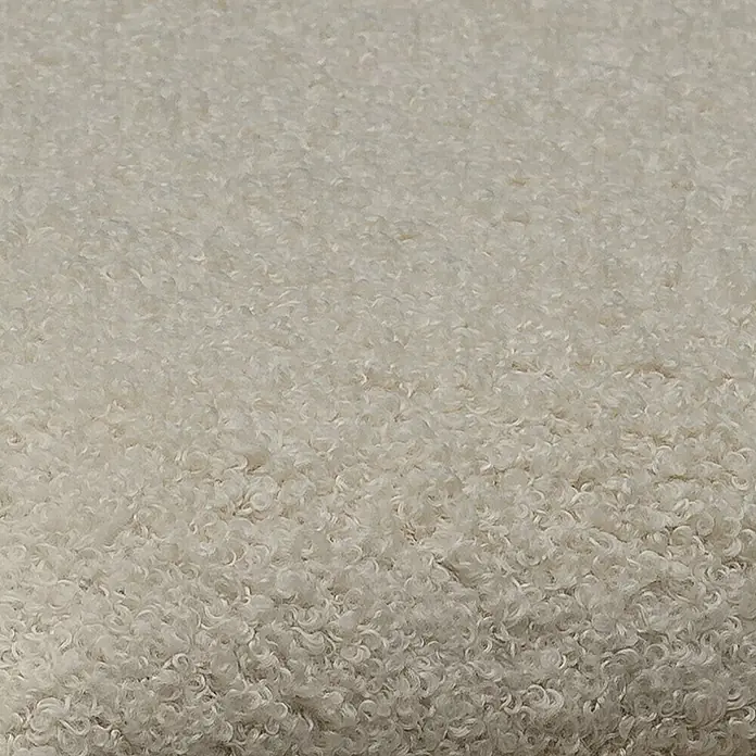 Fllow Wandpolster Wolke - Naturweiß, 60 x 30 cm - Nahaufnahme eines weichen, beigen Schaffellteppichs. Die Textur ist dicht und lockig und bietet eine gemütliche und einladende Oberfläche.
