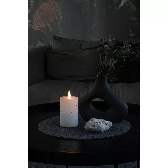 Konstsmide LED-Kerze - Weiß, Höhe: 11,8 cm, 7,5 cm, Wachs - Eine weiße LED-Kerze mit Strasssteinen, schwarze Vase mit Disteln und ein Dekorstein auf einem dunklen Couchtisch.