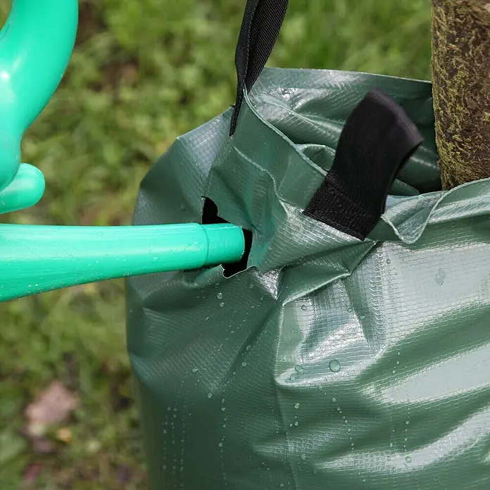 Floraworld Bewässerungssack Comfort - Passend für: Bäume bis Ø 18 cm, 400 g/m² - Ein grüner Bewässerungssack wird mit einer grünen Gießkanne befüllt, um einen Baum langsam und effizient mit Wasser zu versorgen.