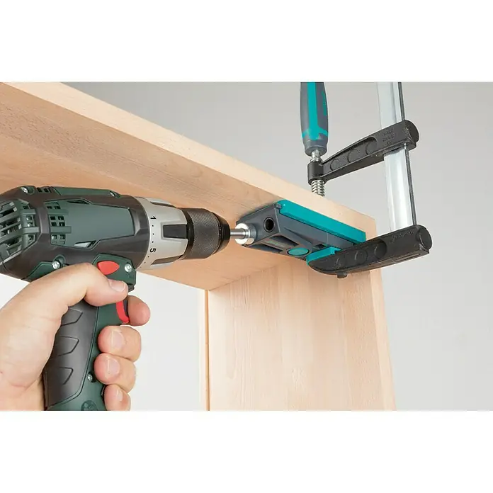 Wolfcraft Maletín de herramientas Undercover Jig Torx - 54 pzs. - Un taladro perfora un agujero en una tabla de madera utilizando una plantilla de perforación fijada con una abrazadera.