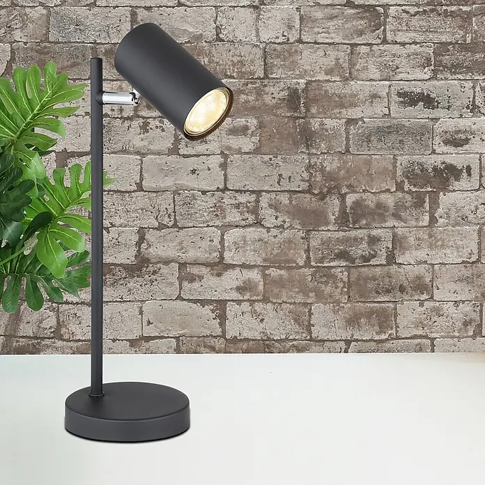 Globo Lámpara de sobremesa Robby - Ø x Al: 12 x 35 cm, GU10 - Elegante lámpara de mesa en negro mate con foco ajustable y planta decorativa frente a una pared de ladrillos.