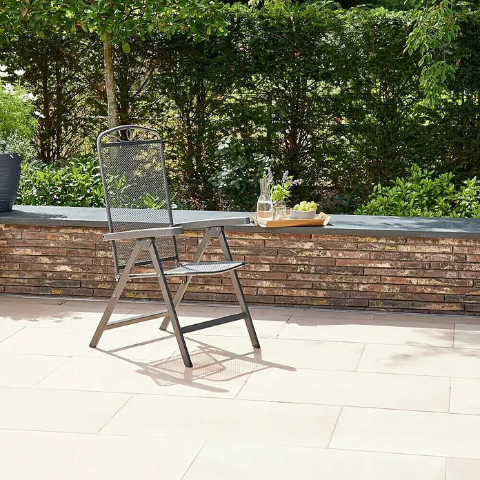 Siena Garden Elda Klappstuhl - Klappbar, Anthrazit, B x T x H: 65 x 60 x 103 cm - Ein grauer, klappbarer Metallstuhl mit Netzmuster steht im Garten. Im Hintergrund Mauer, Pflanzen und ein Tablett mit Getränken und Obst.