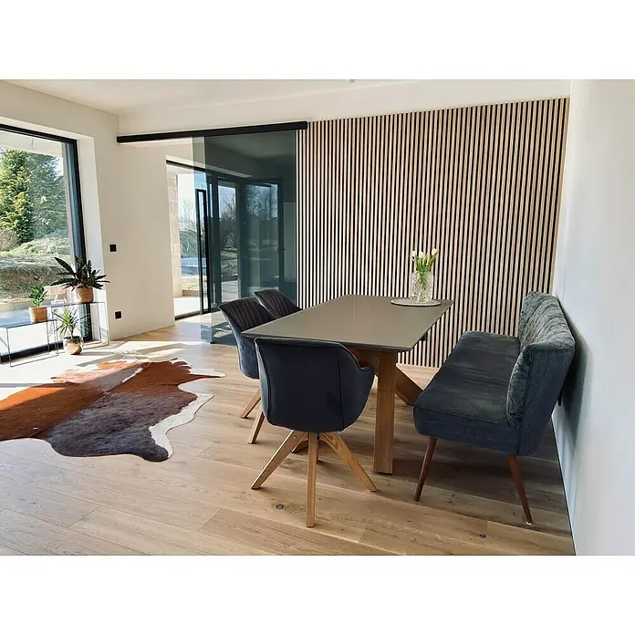 FibroTech Akustikpaneel Premium - Light Oak, 2.440 x 605 x 22 mm - Helles Esszimmer mit Holzboden, einem Esstisch mit Stühlen und einer Bank sowie einer dekorativen Holzvertäfelung an der Wand.