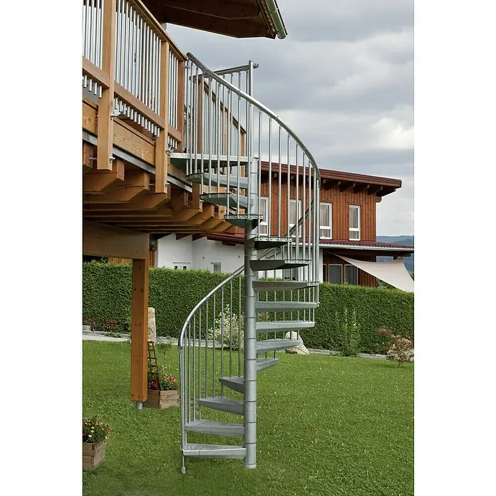 Minka Außentreppe Rondo Zink Plus - Durchmesser: 160 cm, Geschosshöhe: 300 cm, Anzahl Steigungen: 13 Stk. - Eine elegante Wendeltreppe aus Metall führt von einer hölzernen Terrasse in den Garten. Die Treppe ist ein echter Hingucker und bietet einen stilvollen Zugang.