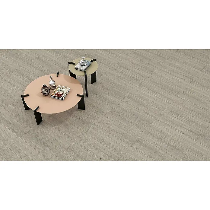 Laminado Roble Vivaldi - 1.202 x 195 x 12 mm, AC5 - Interior elegante con suelo de vinilo gris claro que crea un ambiente cálido y acogedor. Mesas redondas con decoraciones complementan el diseño moderno.