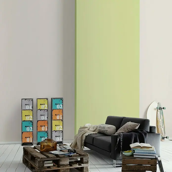 A.S. Création Vliestapete Glatte Wand Meistervlies 5 - Grau, Uni, 10,05 x 0,53 m - Einrichtungsidee mit einem schwarzen Sofa, einem Couchtisch aus Paletten und bunten Schubladenelementen im Wohnzimmer.