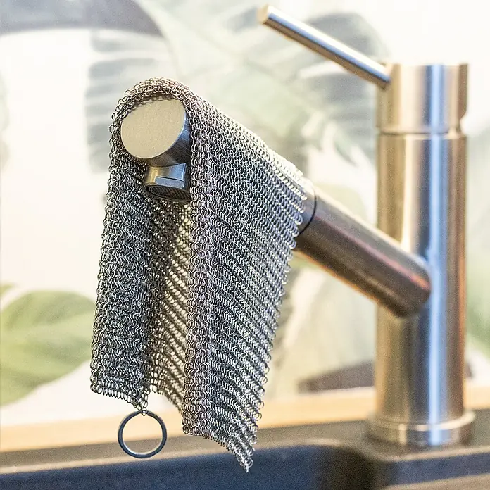 Grillreiniger Ringreiniger - L x B: 20 x 20 cm, Edelstahl - Nahaufnahme eines Spültischhahns mit einem Kettenhemd-Topfreiniger, der darüber hängt, der ein praktisches und stilvolles Küchenaccessoire darstellt.