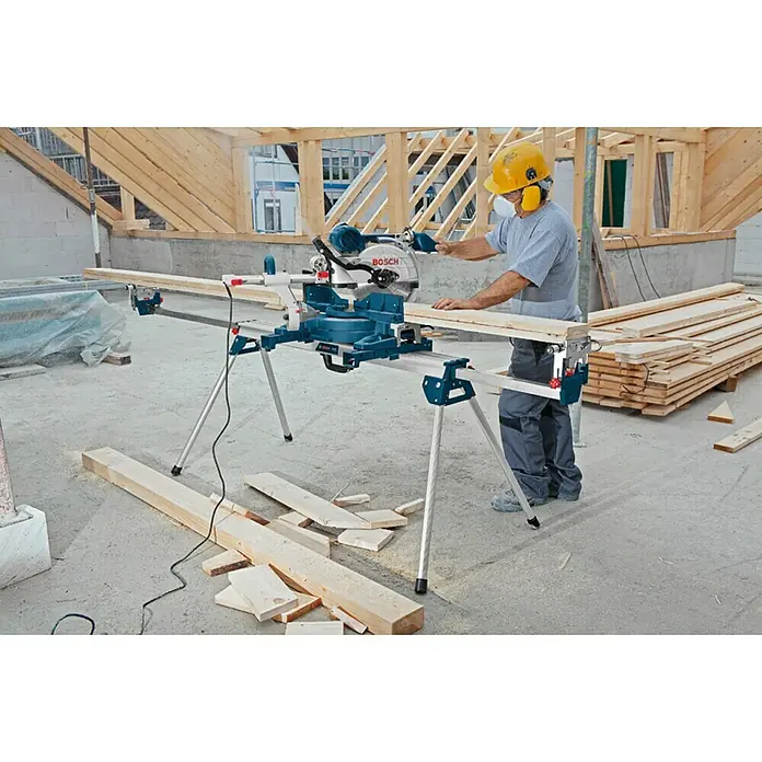 Bosch Professional Transport- & Arbeitstisch GTA 3800 - Arbeitshöhe: 824 mm, Traglast: 250 kg, Geeignet für: Kappsägen - Ein Bauarbeiter benutzt eine Bosch Kapp- und Gehrungssäge mit Untergestell auf einer Baustelle, um ein Holzbrett zu schneiden.