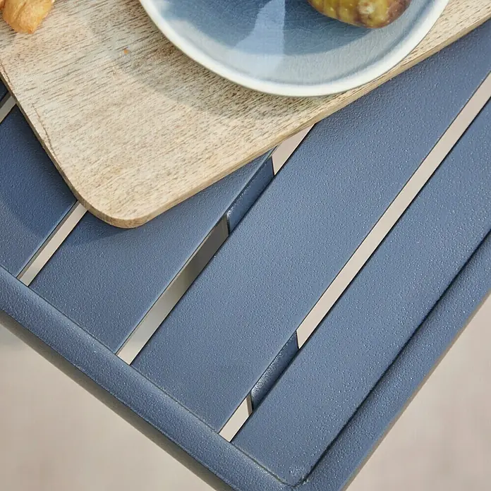 Siena Garden Garten-Beistelltisch AlexisL x B x H: 70 x 70 x 45 cm, Anthrazit matt, Aluminium, Pulverbeschichtet - Nahaufnahme eines blauen Gartentisches mit Holzbrett und Teller, ideal für entspannte Stunden im Freien.