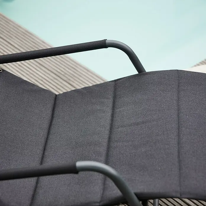 Siena Garden Gartenliege Aliano - Schwarz, Stahl, Pulverbeschichtet - Detailaufnahme eines schwarzen Outdoor-Stuhls mit Armlehnen vor dem Hintergrund eines Pools.