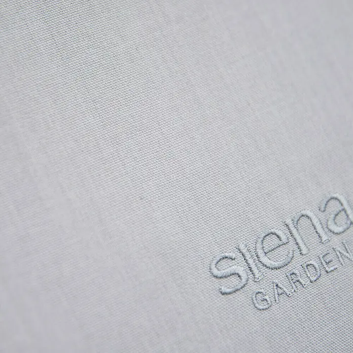 Siena Garden Garten-Schaukelliege AlianoHellgrau, L x B x H: 143 x 57 x 84 cm, Stahl, Pulverbeschichtet - Nahaufnahme von einem hellgrauen Kissen von Siena Garden mit gesticktem Logo, das für Komfort und Stil im Garten sorgt.