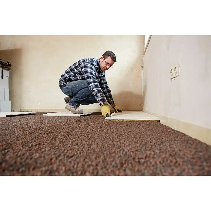 Rigips Rigidur Estrichelement MW - 1.500 x 500 x 30 mm - Mann verlegt Laminatboden mit Steinteppich-Optik in einem Raum. Der Bodenbelag wird professionell verarbeitet, um ein schönes Finish zu erzielen.