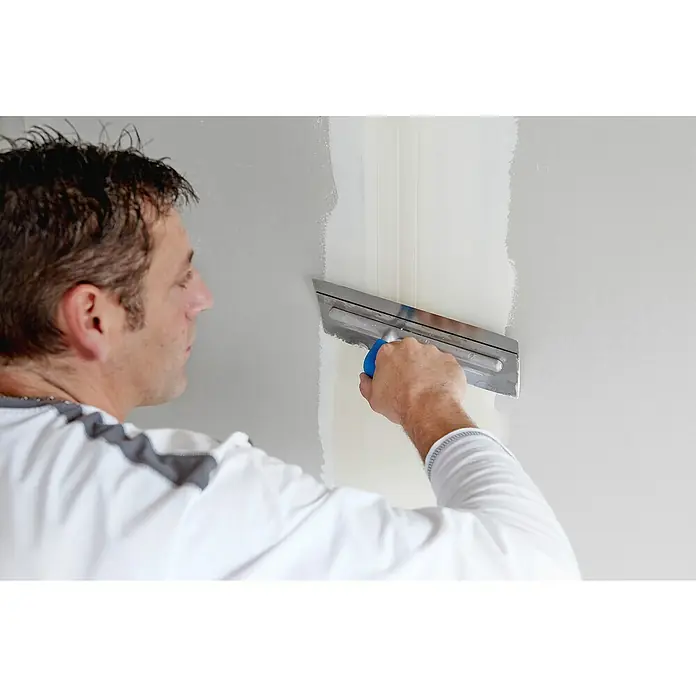 Rigips Fugenspachtel ProMix Plus - 5 kg - Ein Mann glättet Spachtelmasse mit einer Glättkelle an einer Wand, um eine ebene Fläche zu schaffen. Das Werkzeug ist entscheidend für ein professionelles Finish.