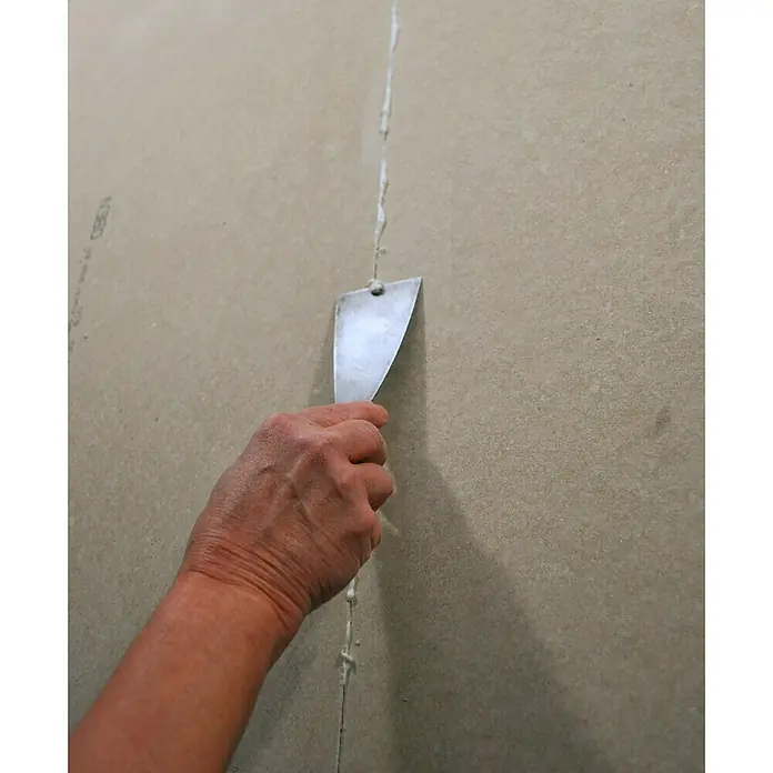 Rigips Rigidur Fugenkleber Nature Line - 310 ml - Eine Hand verspachtelt eine Gipskartonwand mit einem Spachtel, um eine glatte Oberfläche zu erzielen. Professionelle Vorbereitung für Malerarbeiten.