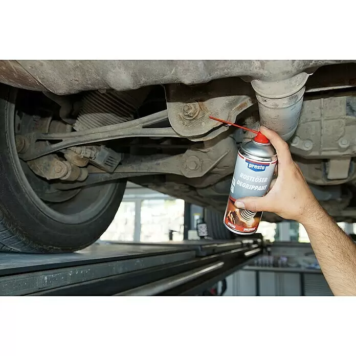 Presto Rostlöser - 400 ml - Eine Hand sprüht Presto Rostlöser aus einer silbernen Dose mit rotem Sprührohr auf eine rostige Autoschraube.