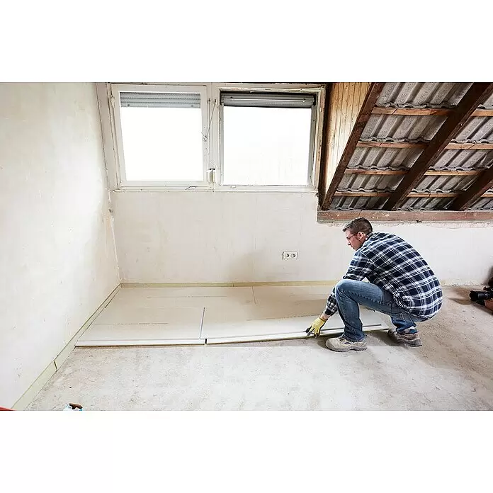Rigips Rigidur Estrichelement HF - 1.500 x 500 x 30 mm - Ein Mann verlegt beige Fußboden-Dämmplatten in einem renovierten Raum.