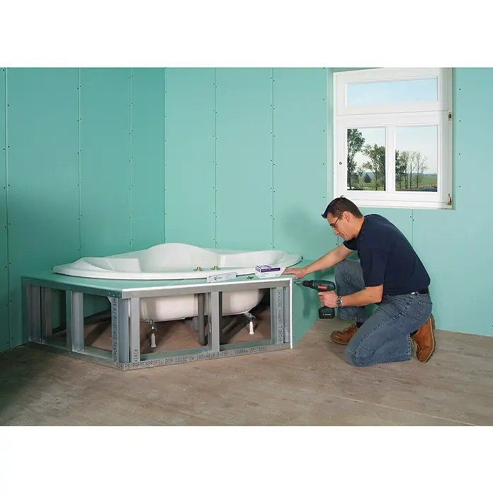 Rigips Gipskartonplatte - 2.600 x 600 x 12,5 mm, Imprägniert - Ein Mann montiert eine Badewanne mit grünen Paneelen und einem Metallrahmen, wobei der Fokus auf dem Installationsprozess und den Baumaterialien liegt.