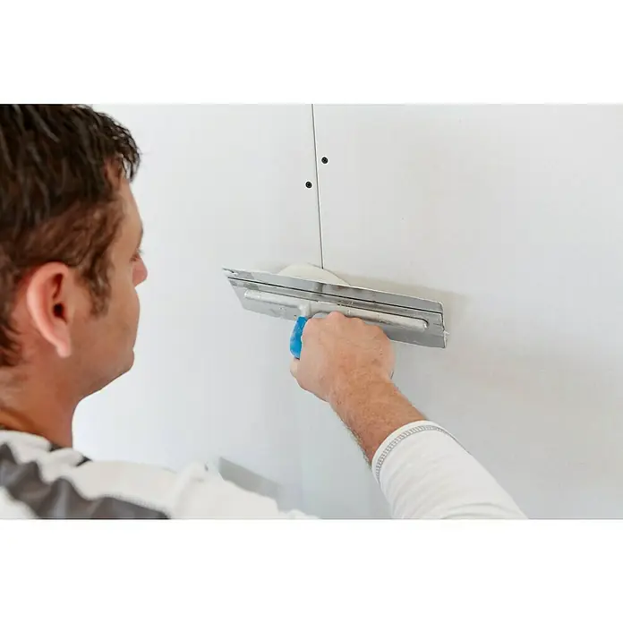 Rigips Fugenspachtel Super - 25 kg - Ein Handwerker verwendet eine Glättkelle, um Spachtelmasse auf eine weiße Wand aufzutragen. Das Werkzeug ist essenziell für glatte Oberflächen.