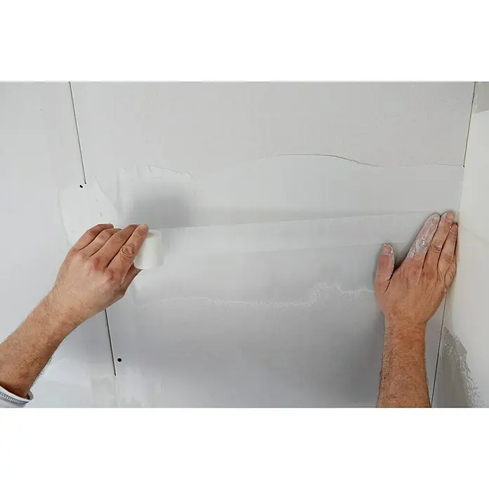 Rigips Fugenspachtel Super - 25 kg - Close-up einer Person, die Malerkrepp an einer Wand anbringt, um eine saubere Kante für Malerarbeiten zu gewährleisten.