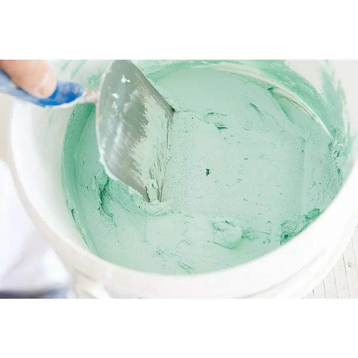 Rigips VARIO Fugenspachtel - 2,5 kg, Imprägniert - Nahaufnahme von Spachtelmasse in einem Eimer. Die mintgrüne Masse wird mit einem Spachtel bearbeitet und ist bereit für die Verarbeitung.