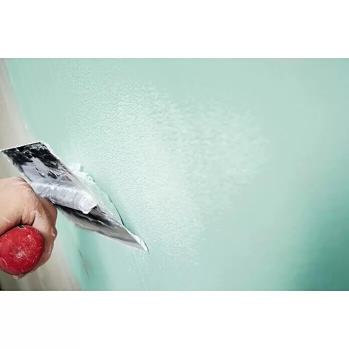 Rigips Haftputzgips Rimat Grün 150 - 25 kg, Gips - Hand mit rotem Spachtel trägt hellgrünen Putz auf eine Wand auf.